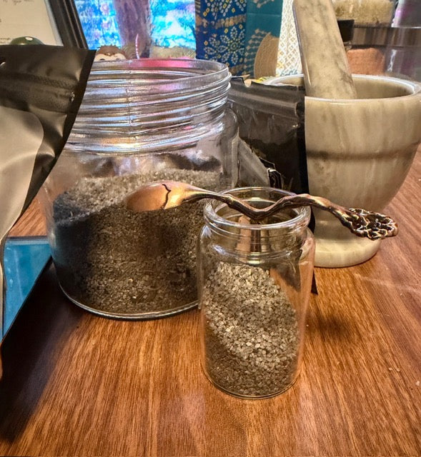 Black witch's salt blend in a glass jar with a wooden scoop and mortar and pestle
