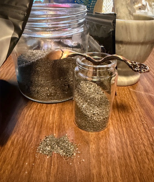 Black witch's salt blend in glass jars with a small amount spilled on a wooden table