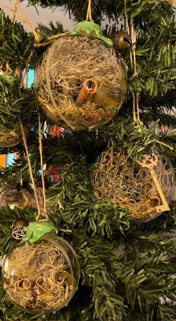 Handmade Witch Balls hanging among evergreen branches, with moss-filled spheres and charms